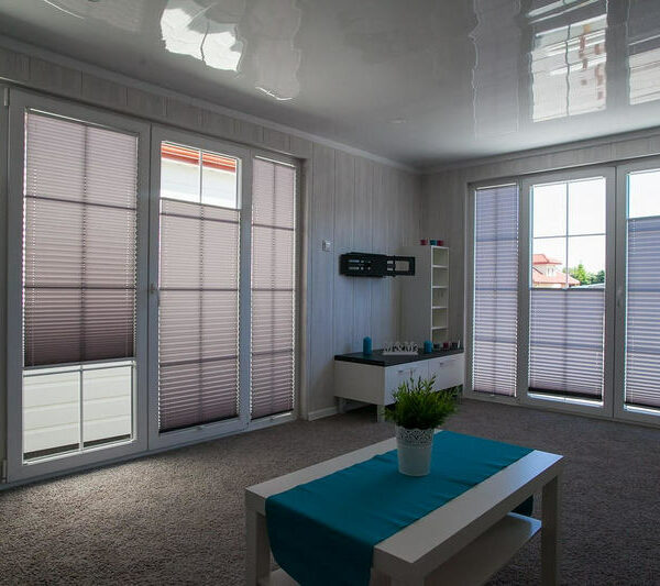 Ein Wohnzimmer mit großen Fenstern, die von Plissees verdunkelt werden.